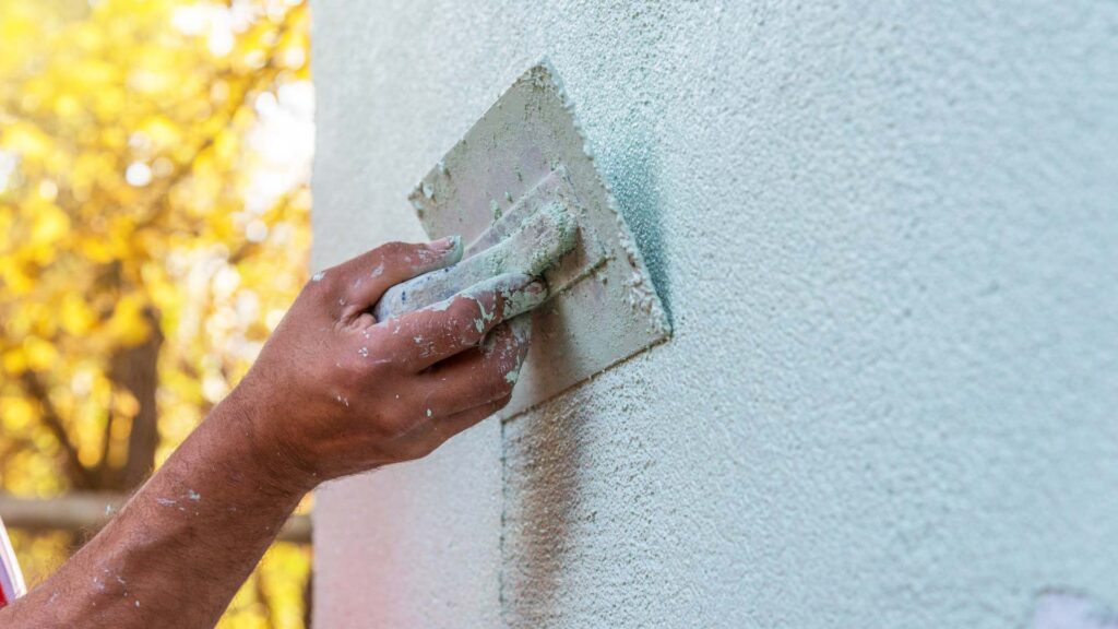 Ein Mann verputzt eine helle Wand mit einer Kelle und konzentriertem Blick