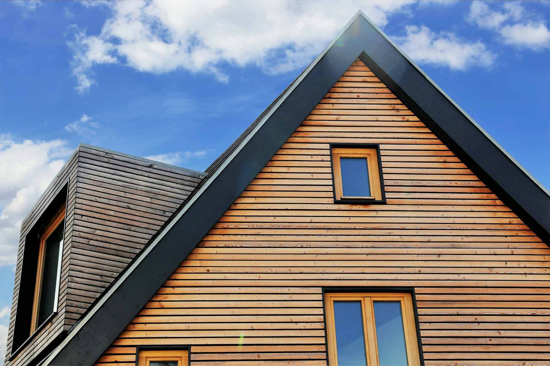 Modernes Holzhaus mit blauer Himmel im Hintergrund, schräges Dach und rechteckige Fenster.