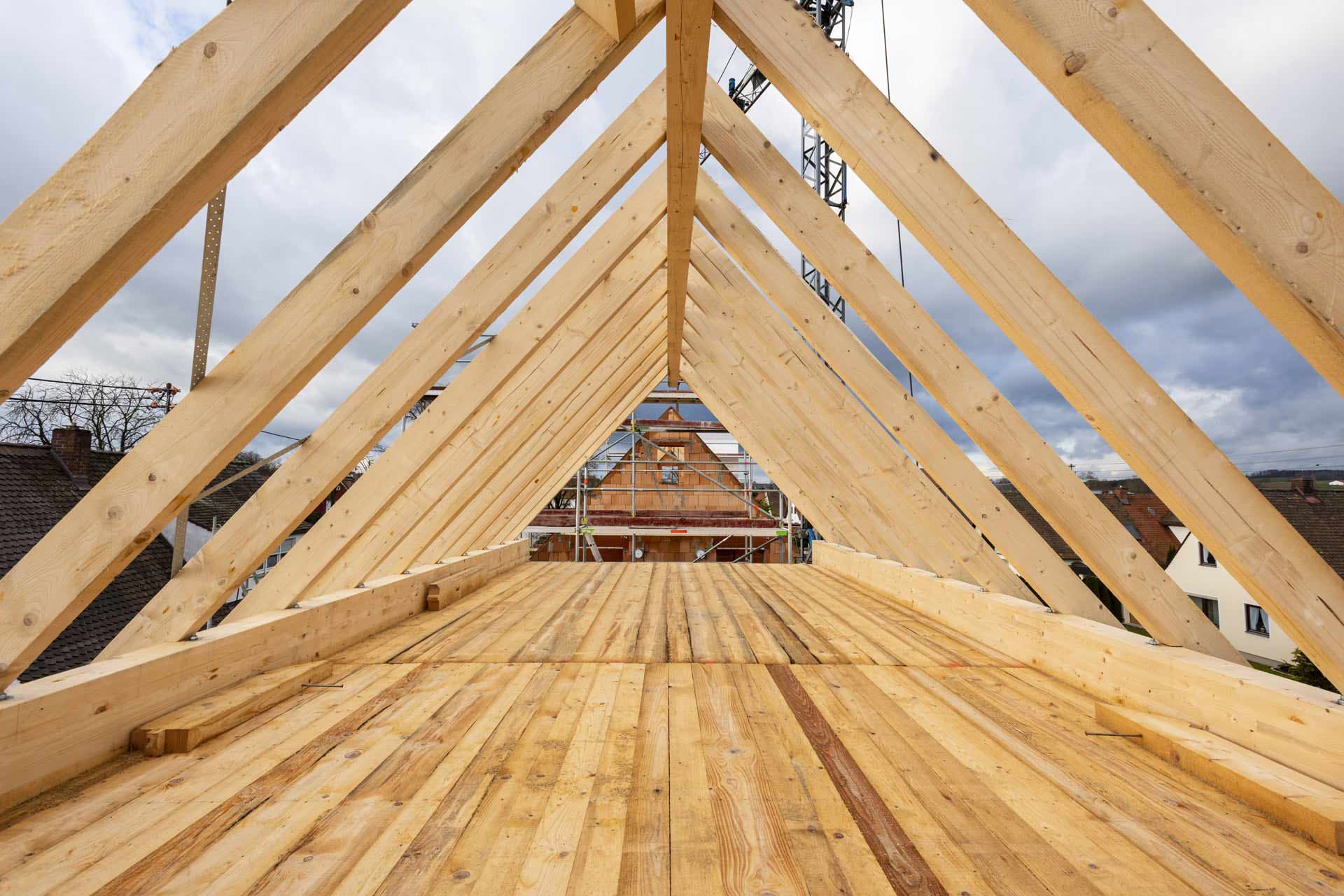 Holzrahmen eines Dachstuhls im Bau, mit hellem Holz und bewölktem Himmel.
